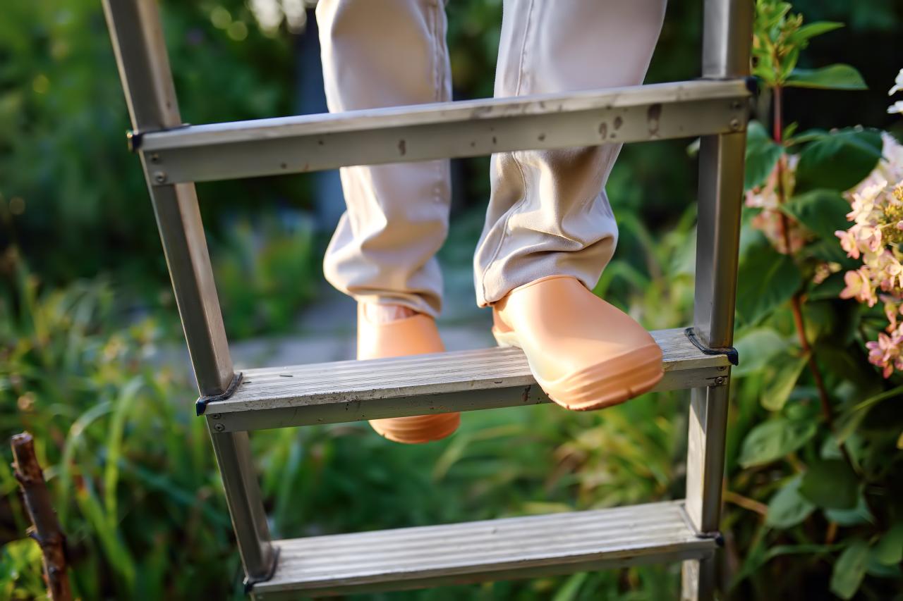 Close-up von einer Person, die mit Gummischuhen eine Gartenleiter besteigt