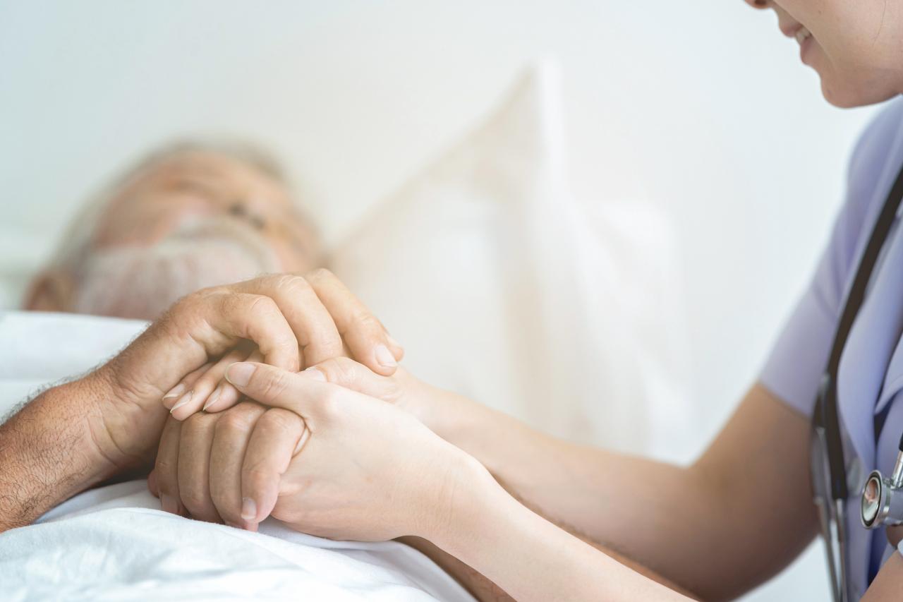 Une auxiliaire de santé tient les mains d'un homme alité.