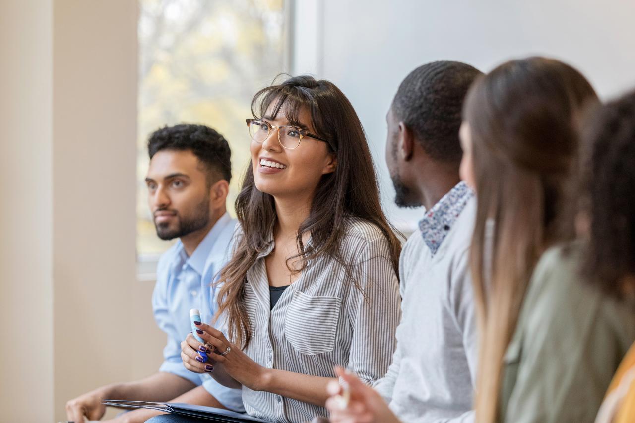 Junge Menschen mit Migrationshintergrund sitzen lachend in einem Klassenzimmer.