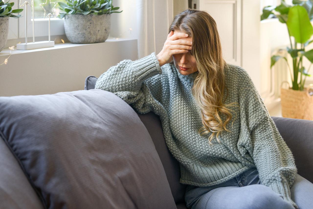 Junge Frau sitzt auf dem Sofa und stützt sich müde mit dem Ellenbogen auf dem Sofa ab