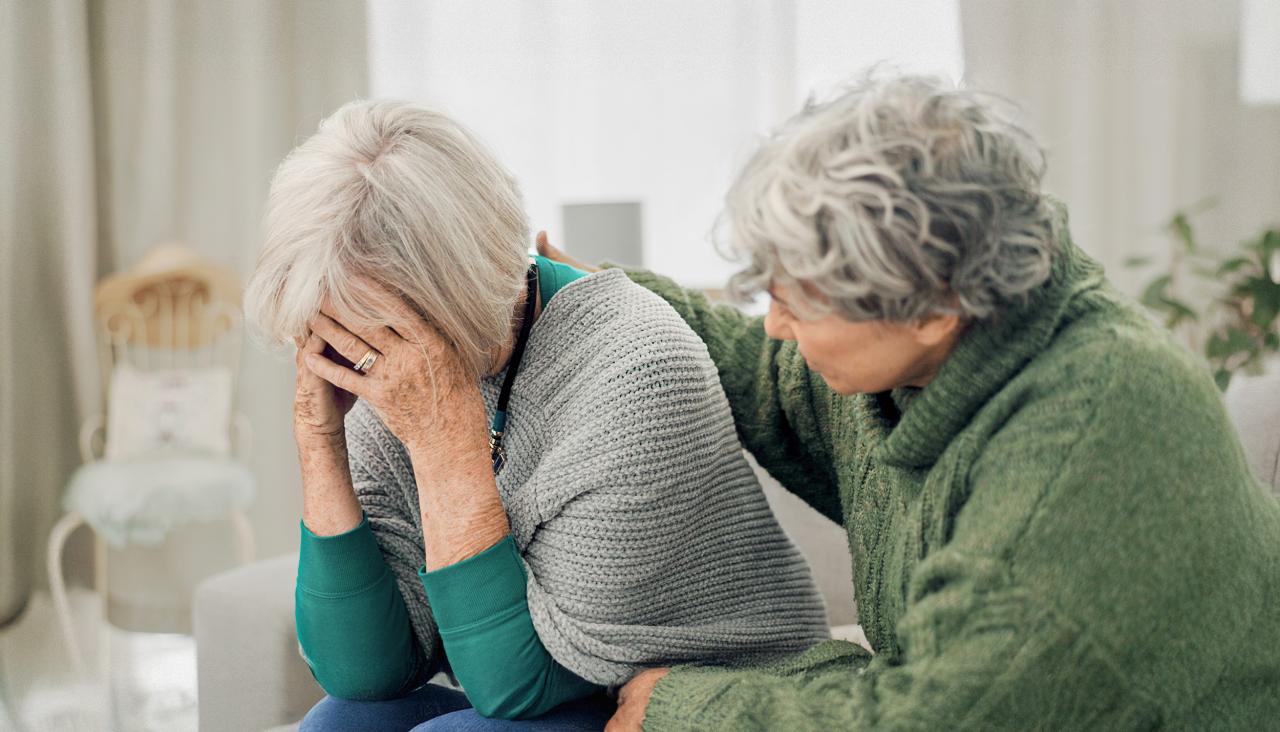 Eine Frau legt einer anderen Frau den Arm auf die Schulter und steht ihr bei