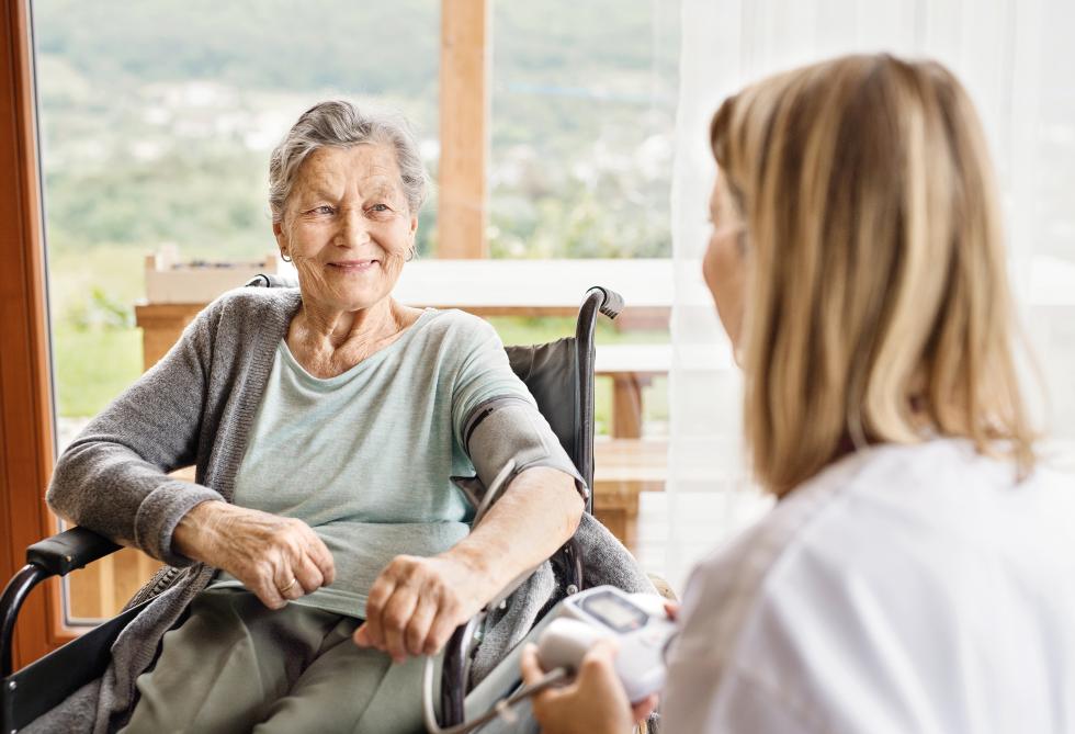 Pflegehelferin spricht mit älterer Frau in Rollstuhl