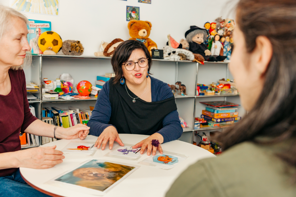 Drei Frauen sitzen an einem Tisch und Besprechen Karten, die vor ihnen auf dem Tisch liegen